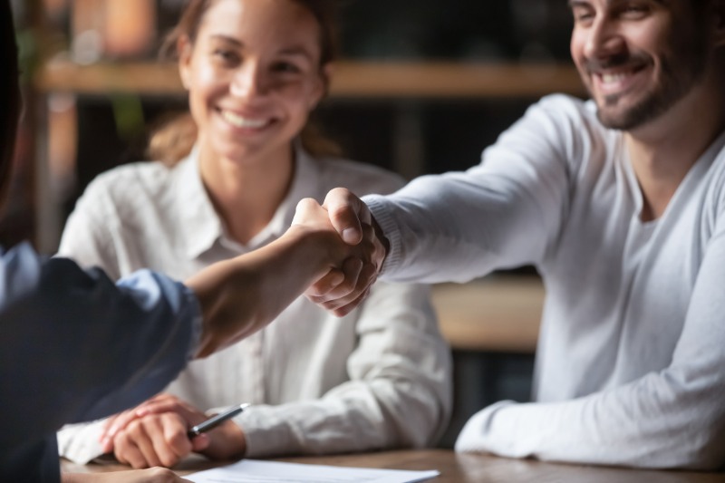 Millennial cheerful business people shaking hands sitting indoors